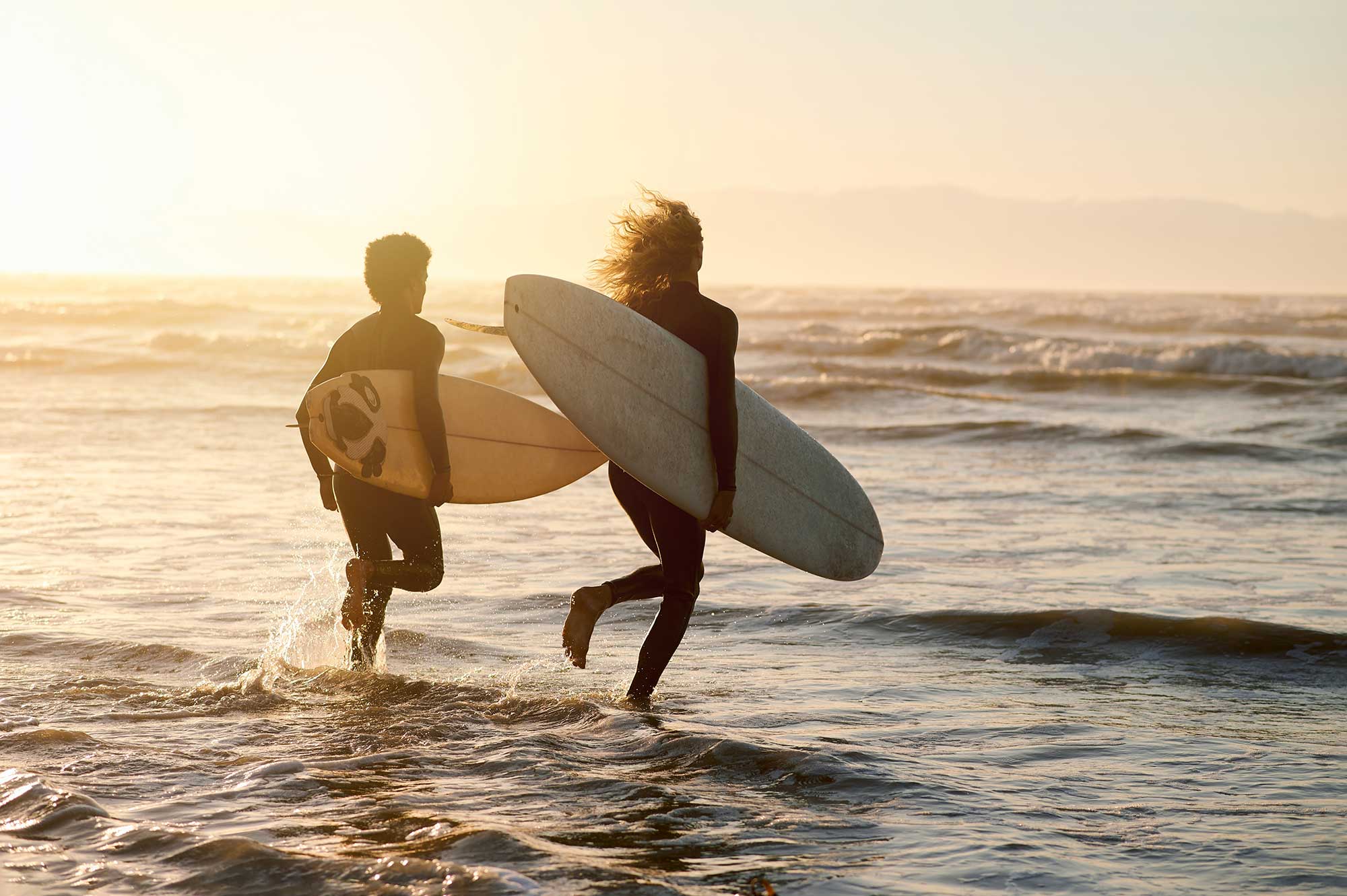 Paar mit Surfbrettern am Strand laufend